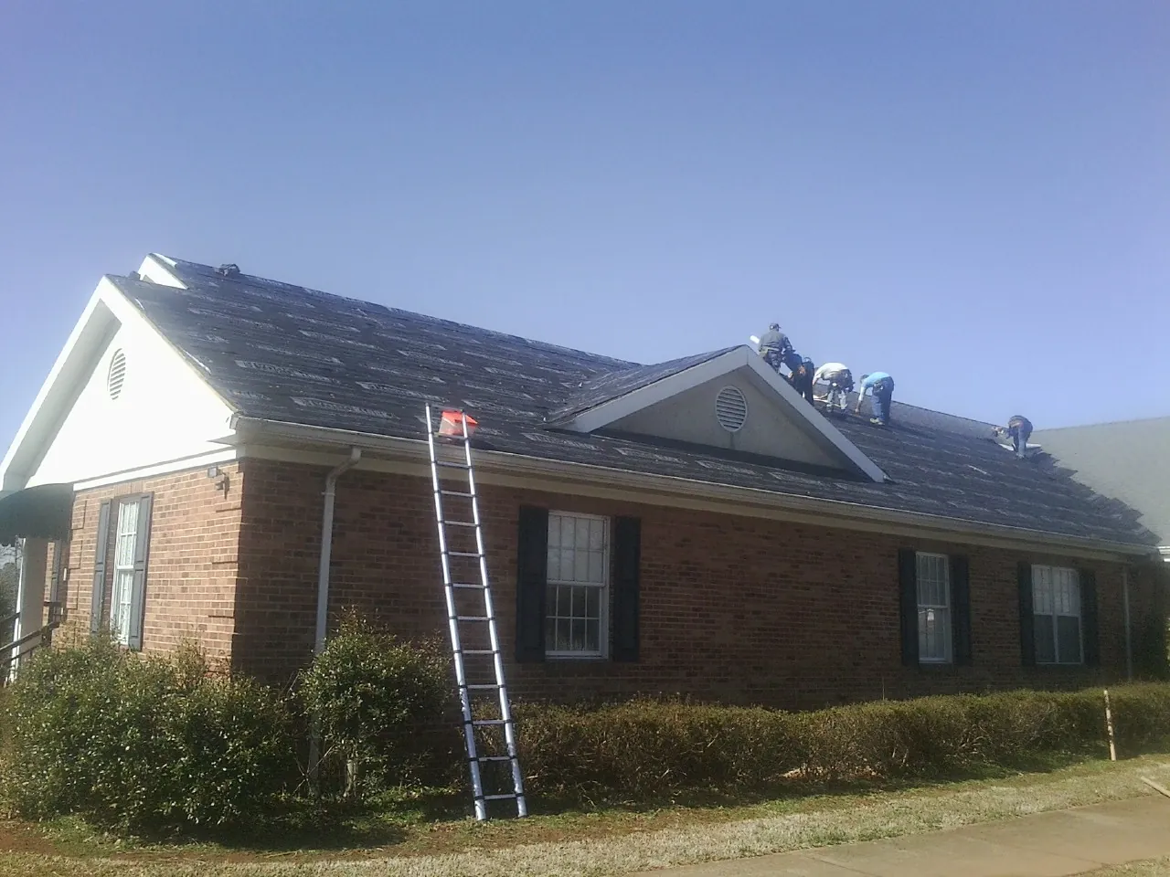 Crew tearing shingles off a brick ranch roof with a ladder set — Emergency Roof Repair work by our crew in East Orleans