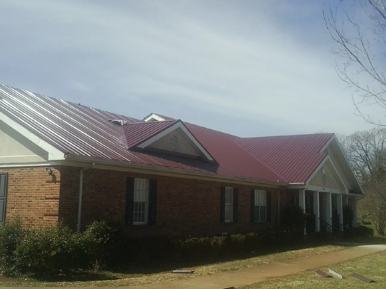Red metal roof with gabled entries on a long brick building, from a Hail Damage Roof Repair job in East Orleans
