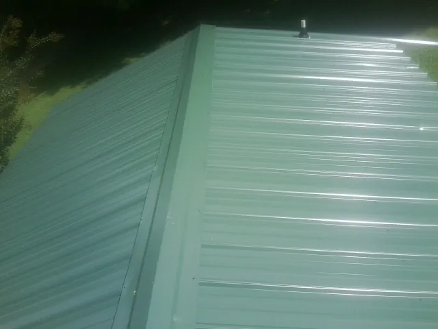New green metal panels meeting at the ridge of a roof — Flat Roof Repair work by our crew in East Orleans