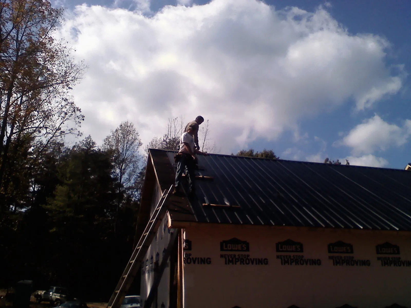 Roofer fastening dark metal panels high against a cloudy sky, from a Roof Inspection job in East Orleans