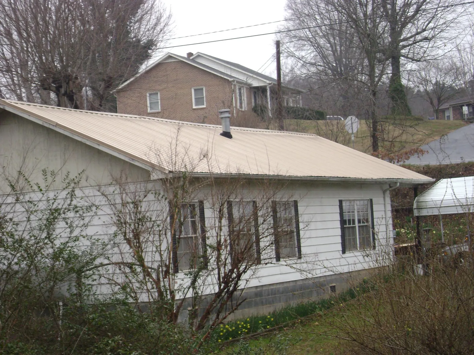 Tan metal roof on a white sided house set into a hillside — Commercial Roofing by Roofing Brothers in East Orleans